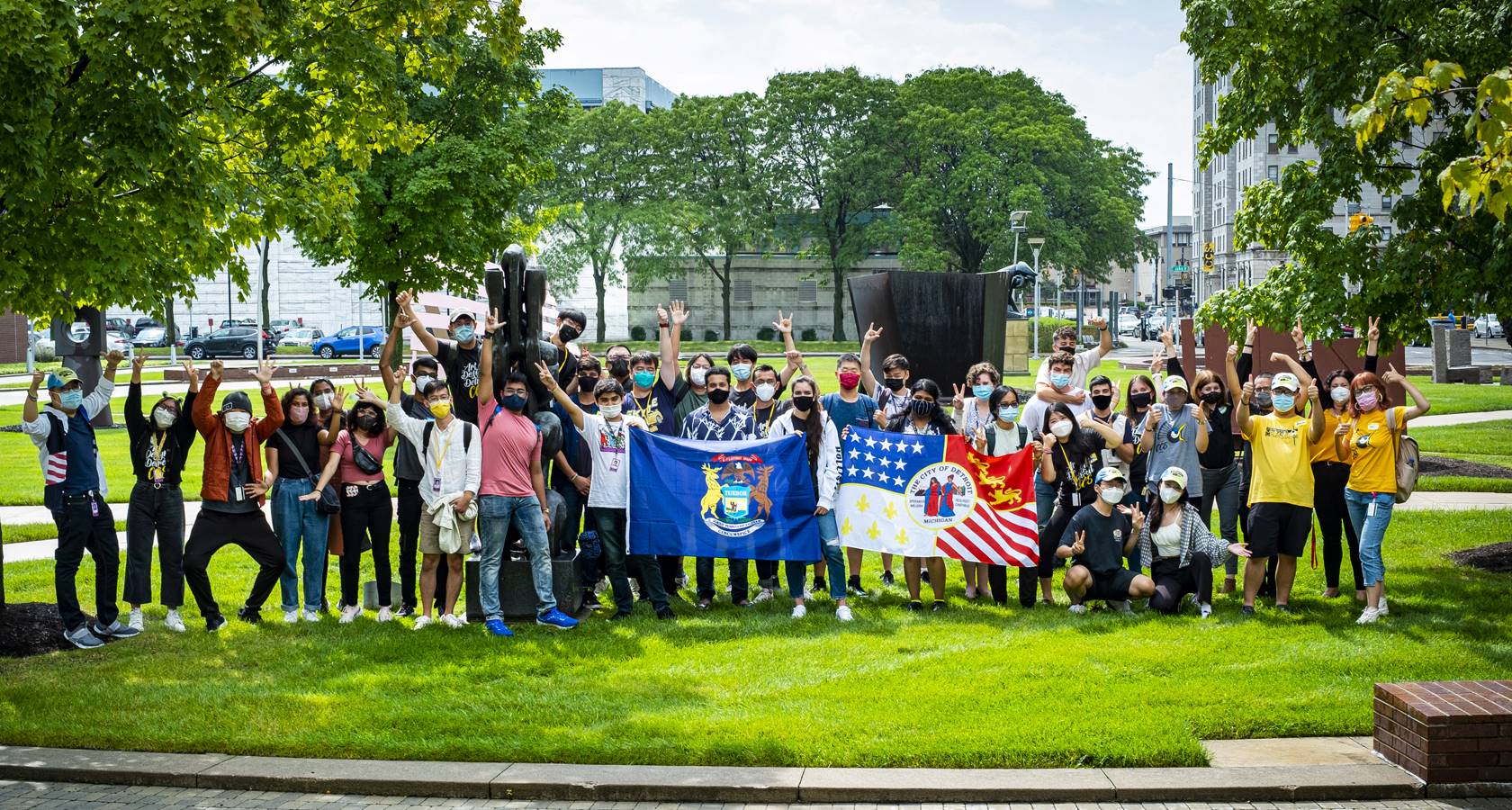 photograph of a diverse group of students holding a city of Detroit flag.