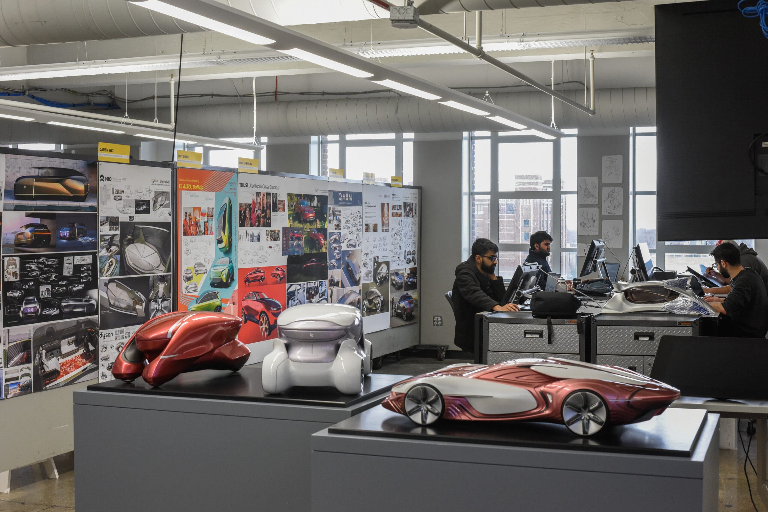 Students using the Transportation Design facilities with model cars in the foreground