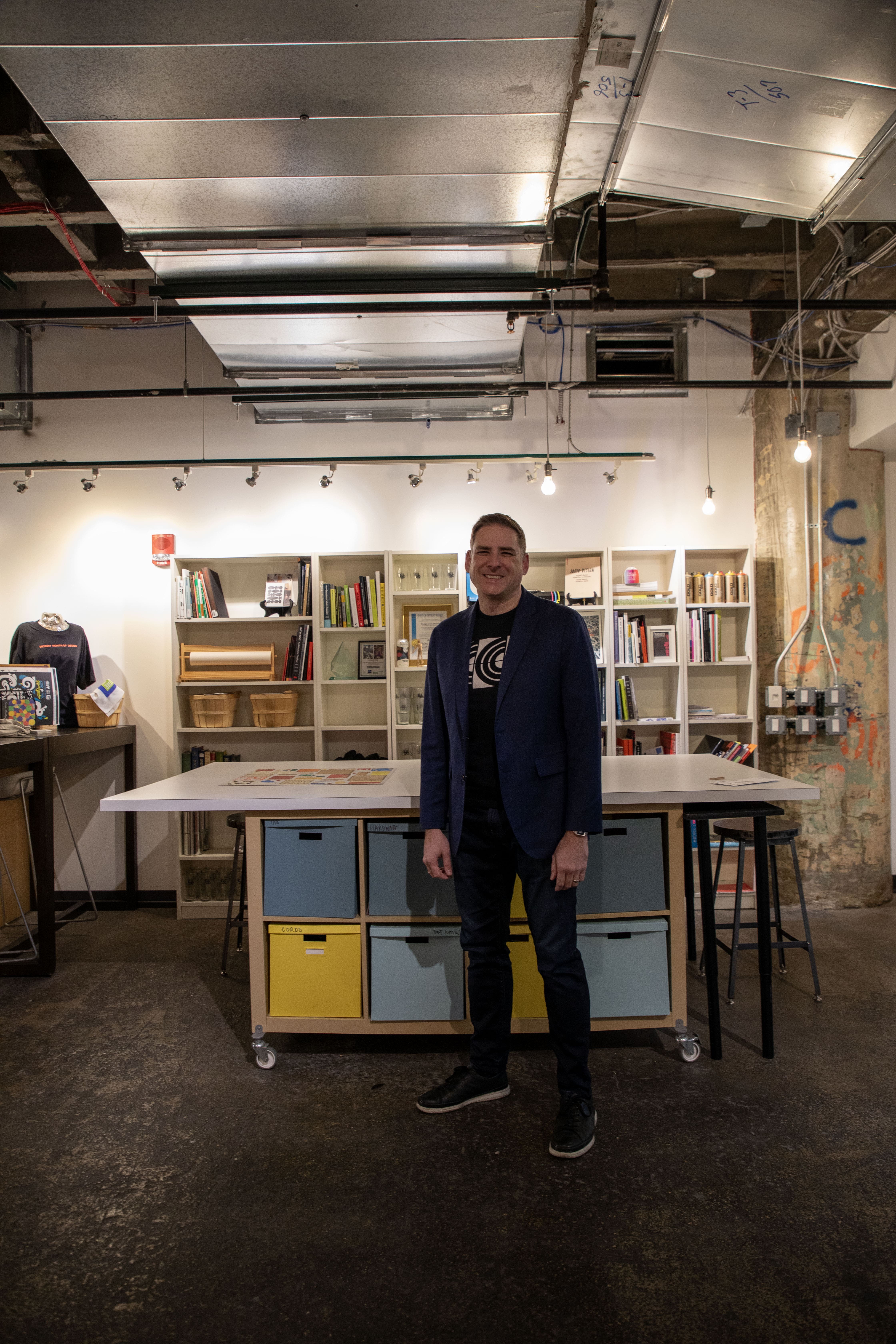 Kevin Gilboe standing in front of large white rectangular table, which is front of a wall of bookshelves.