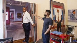 Photo of the artist Mario Moore showing his life sized portrait paintings