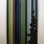 painting of green, white, blue, and grey stripes. To the left are a few stacked grey pebbles