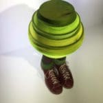 Abstract sculpture of several green discs stacked on top of a pair of brown shoes